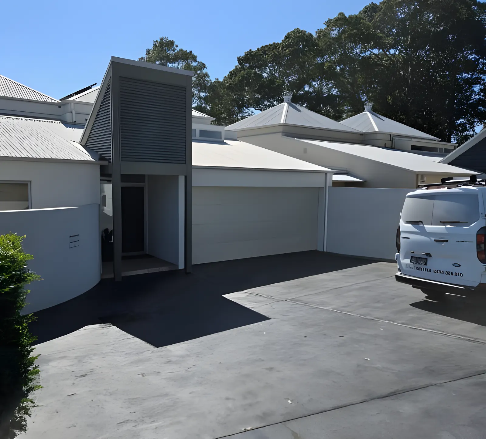 A rendered townhouse and garage front painted white, with the D'luxe van parked out the front